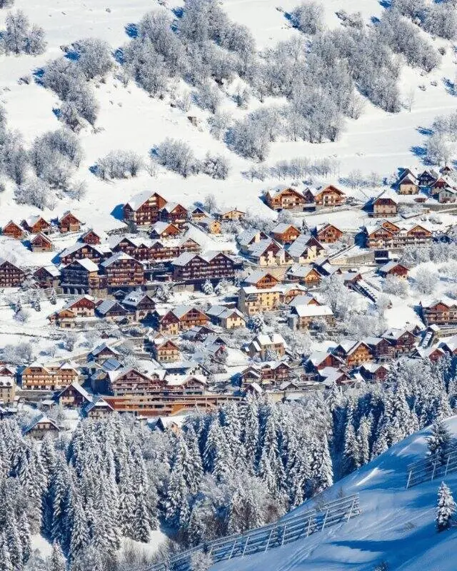 Snow-covered wooden chalets among frosted trees in the Alpe d’Huez area