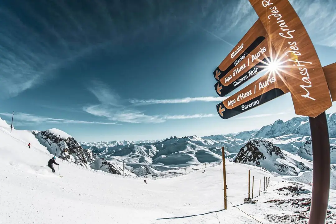 Skiers below a trail sign to the Sarenne run in Alpe d’Huez, Grand Domaine