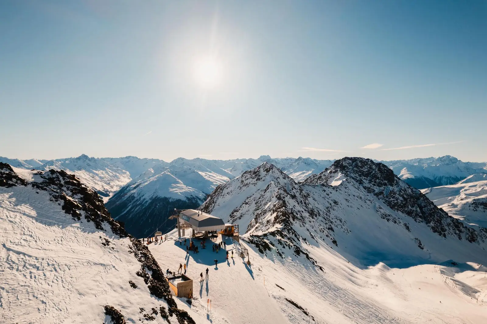 Chairlift summit station above snowy Alpine peaks in winter sunshine