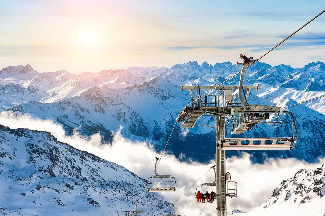 Chairlift above a sea of clouds and snowy high Alpine peaks at sunrise